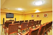 Rows of upholstered chairs arranged facing a wall-mounted TV in a small screening or meeting room.