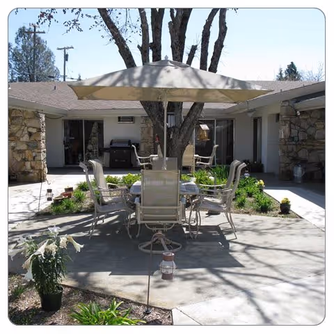 Courtyard patio with a table, umbrella and chairs surrounded by a single-story building and landscaping.