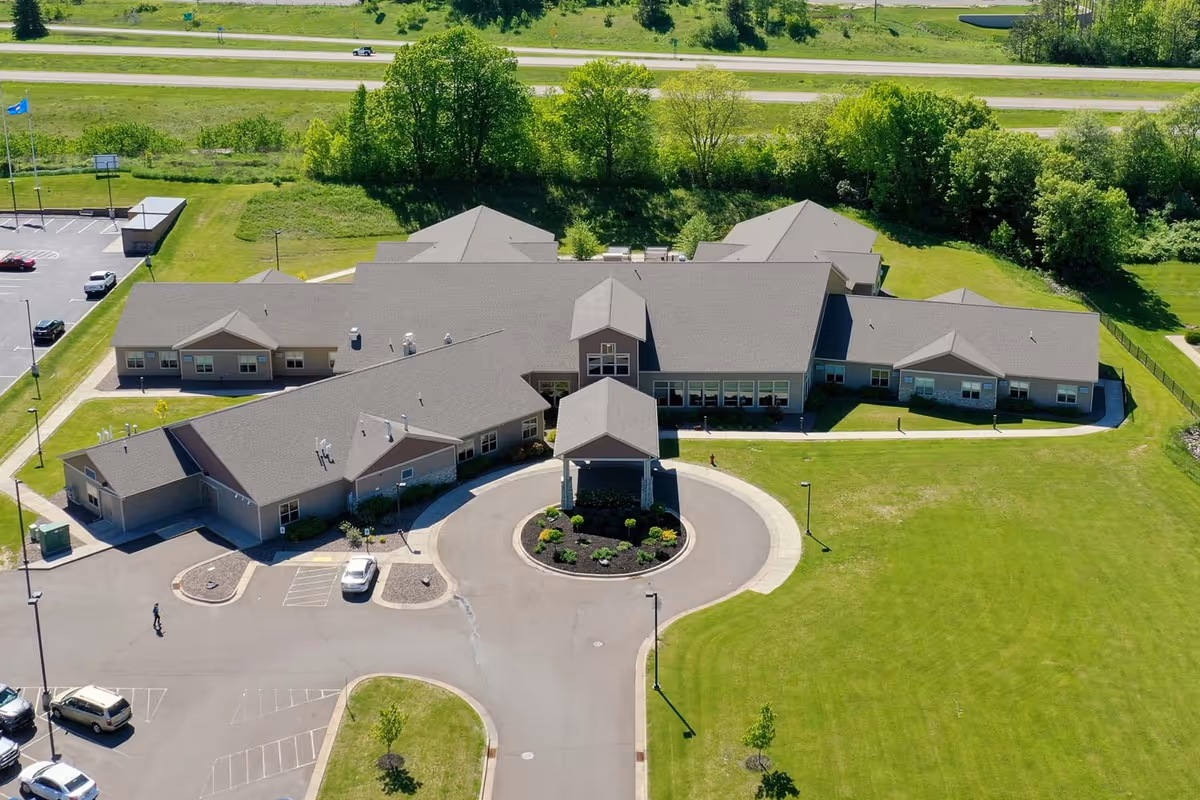 Aerial view of a single-story senior living facility with a circular drive, parking area, and large grassy grounds.