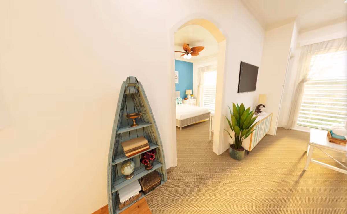 Bright living area with a boat-shaped shelf, potted plant, wall-mounted TV, and an arched doorway opening to a bedroom with a blue accent wall.