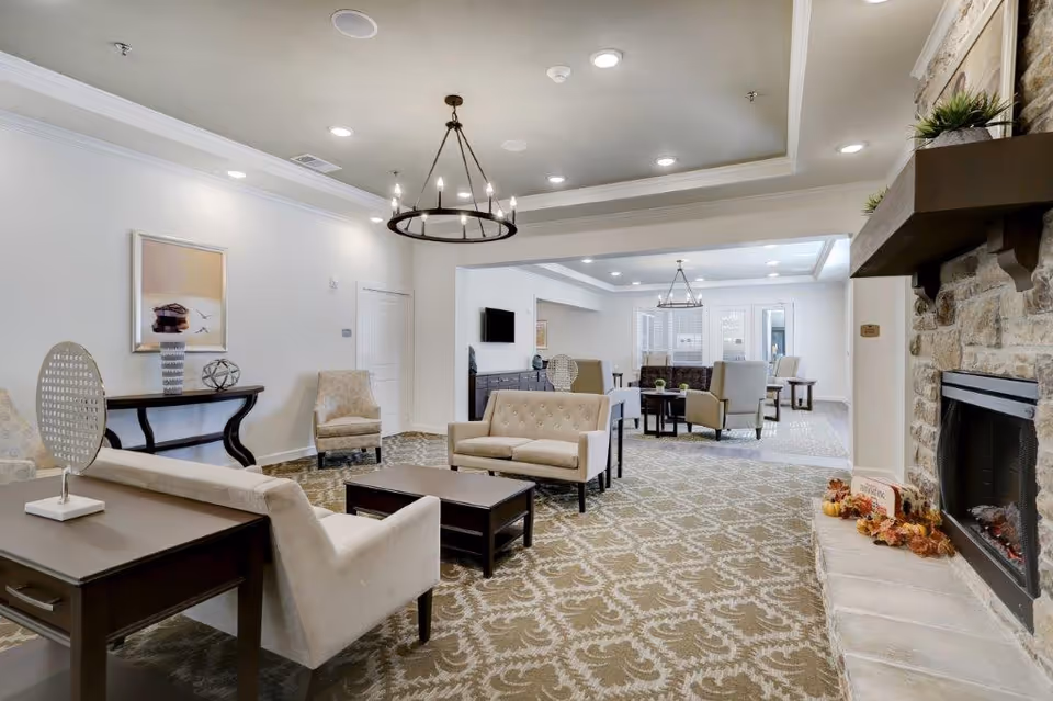 Bright, furnished communal lounge with multiple seating areas, chandeliers, and a stone fireplace.