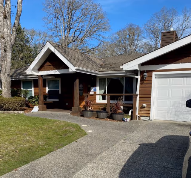 A single-story wooden house with a driveway, front porch, and potted plants.