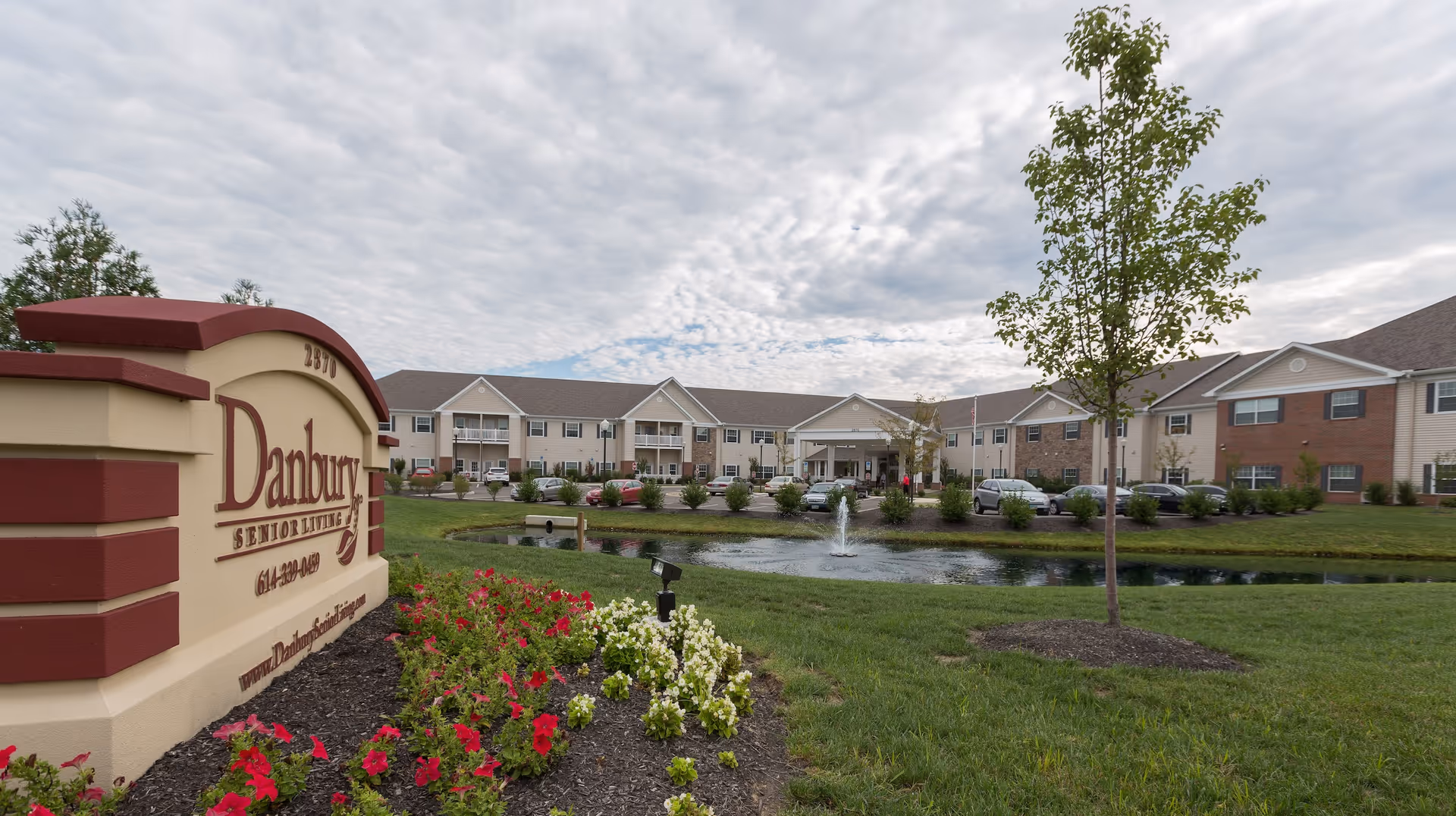 Danbury Senior Living building exterior with front sign, pond, and landscaped beds.