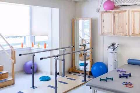 Interior rehab gym at Alpine Healthcare Center with parallel bars, balls, and therapy equipment.