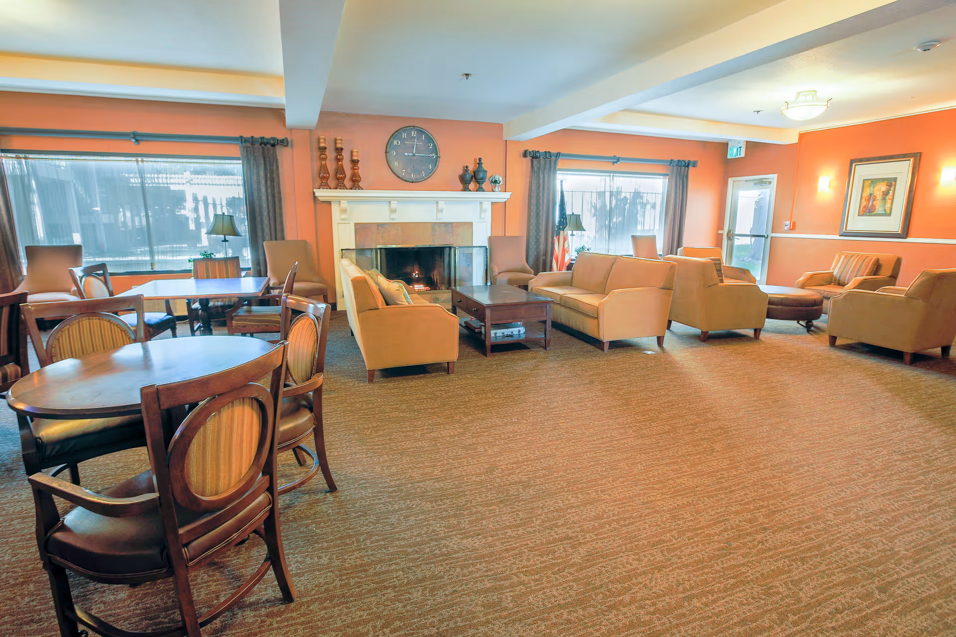 Spacious senior living common lounge with sofas, armchairs, dining tables, a fireplace, and large windows.