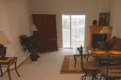 Cozy senior living living room with sofas, chairs, lamps, plants, and sliding glass doors.