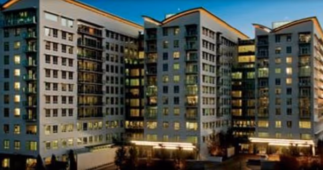 Exterior view of a large multi-story residential building at dusk with many windows illuminated and balconies visible.