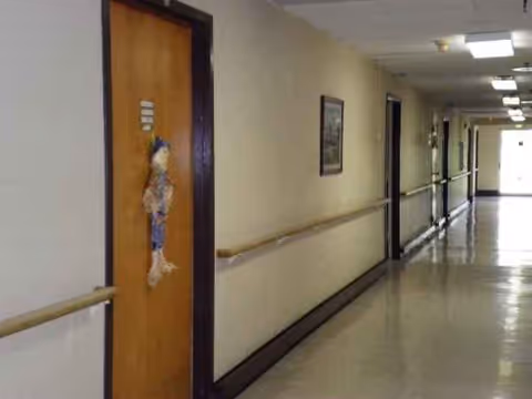 Long corridor inside a senior living facility with doors, handrails, and framed art.