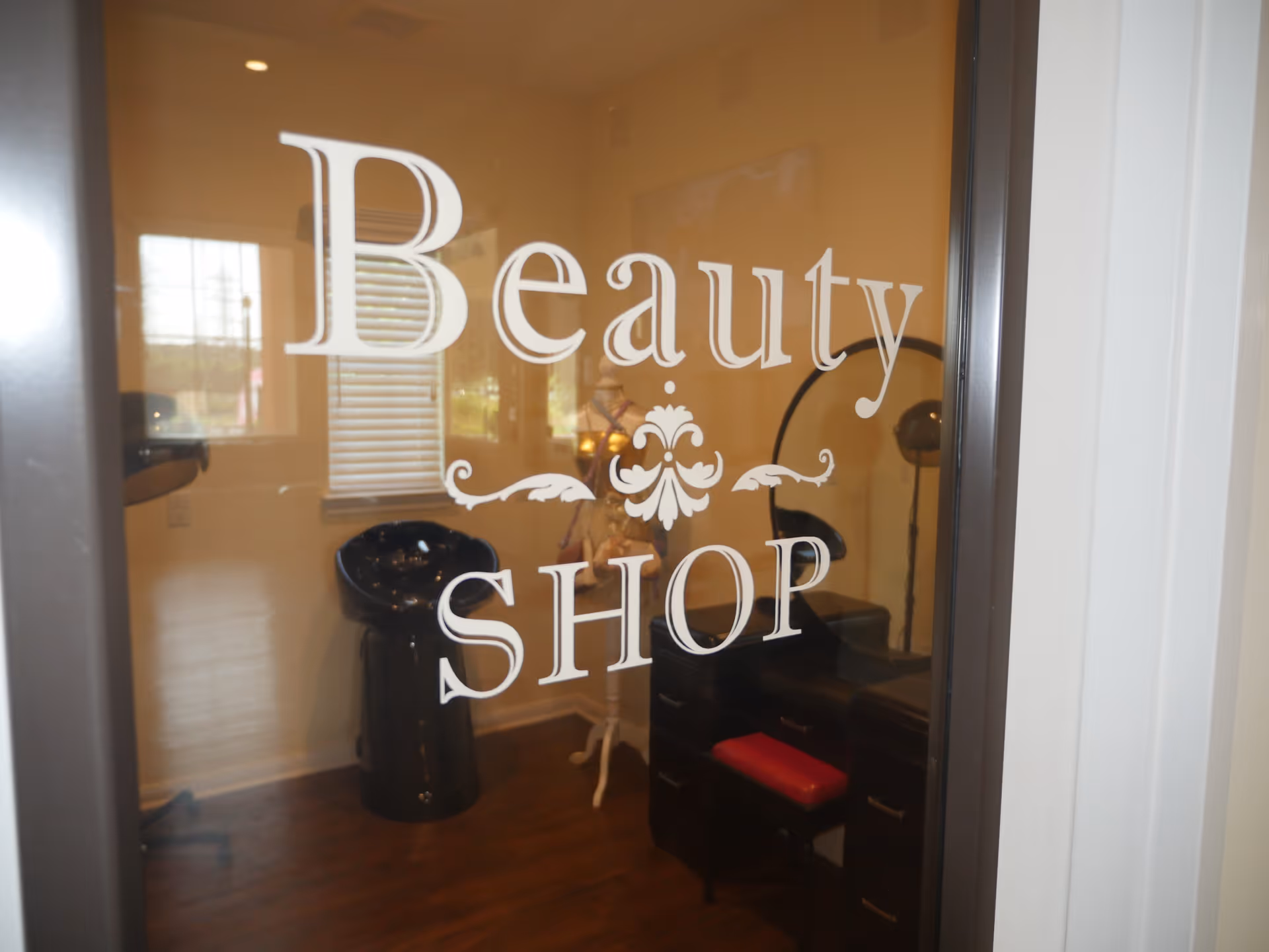 Glass door labeled "Beauty Shop" revealing an interior salon with a shampoo sink, styling chair, and equipment.