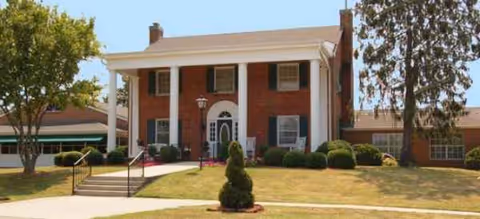 Brick senior living facility entrance with white columns, steps, and landscaped lawn.