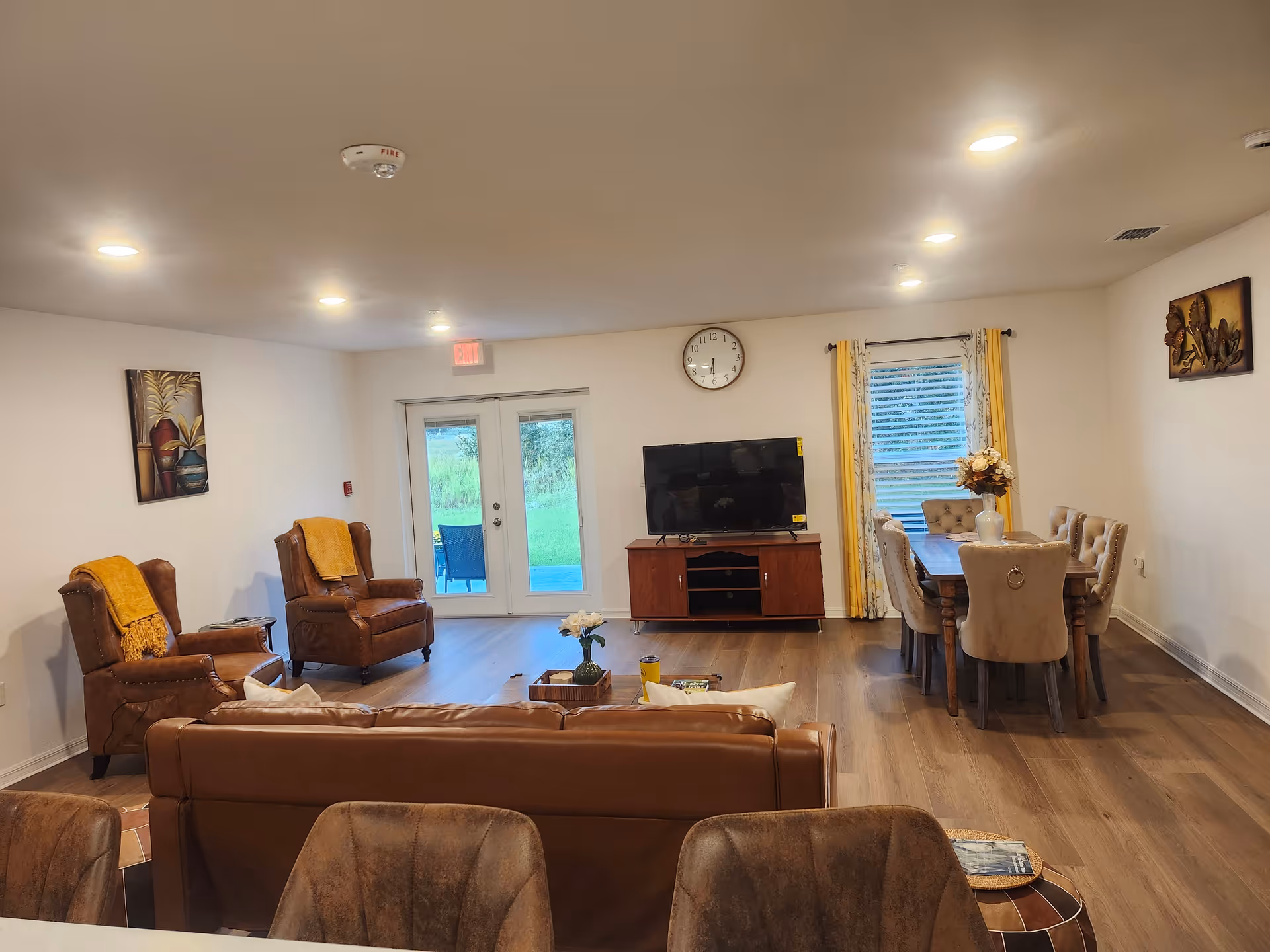 Open living and dining room with leather sofas and armchairs, a TV on a wooden cabinet, and a dining table by a window.