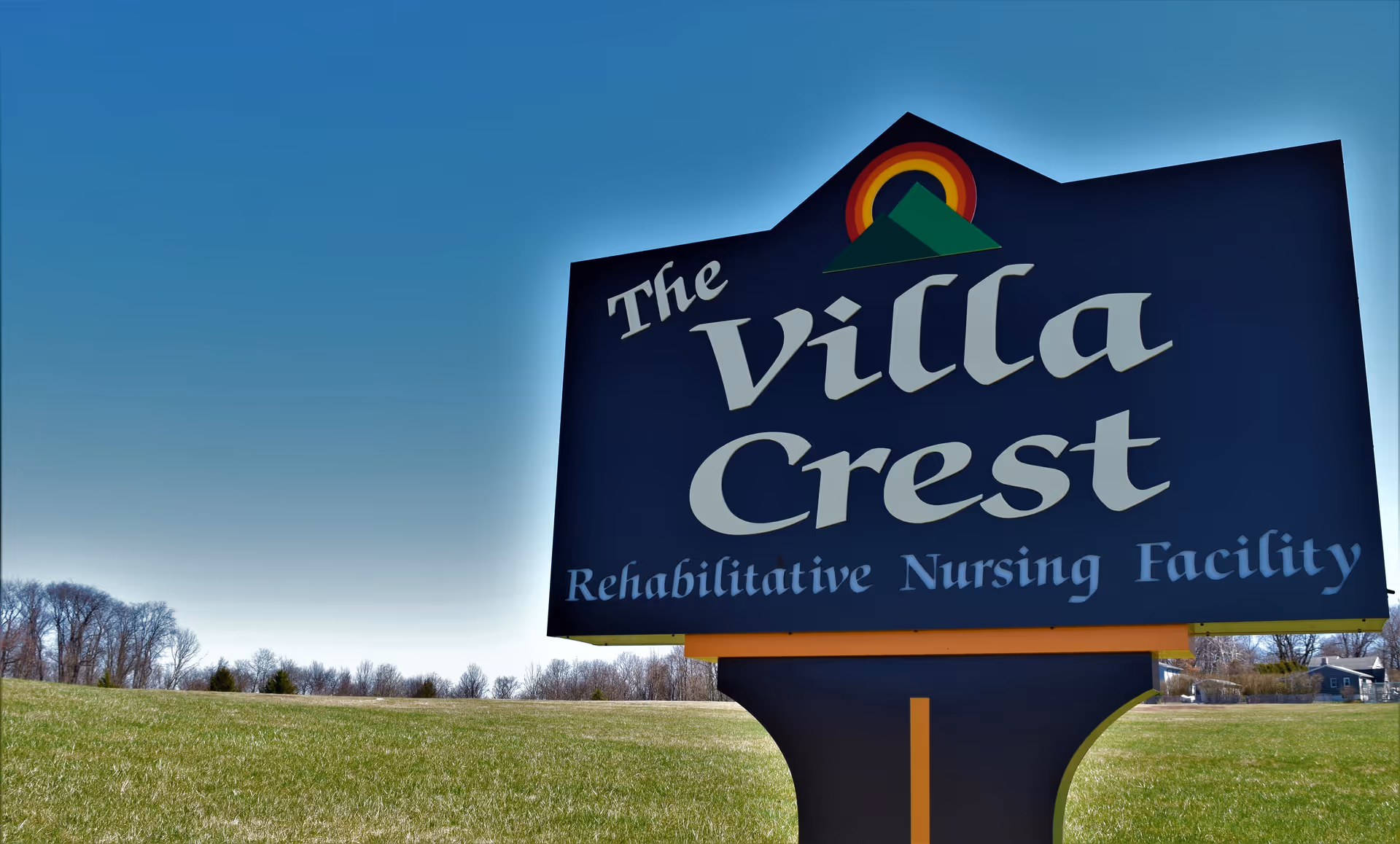 Large roadside sign reading 'The Villa Crest Rehabilitative Nursing Facility' in a grassy field under a clear blue sky.