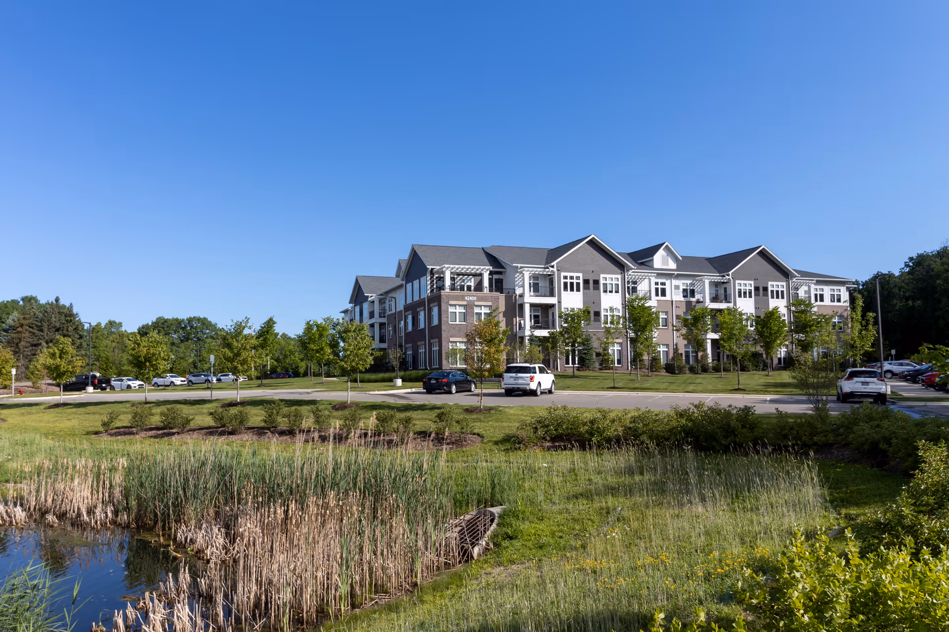 A modern senior living facility with brick facade, parked cars, and green landscaping.