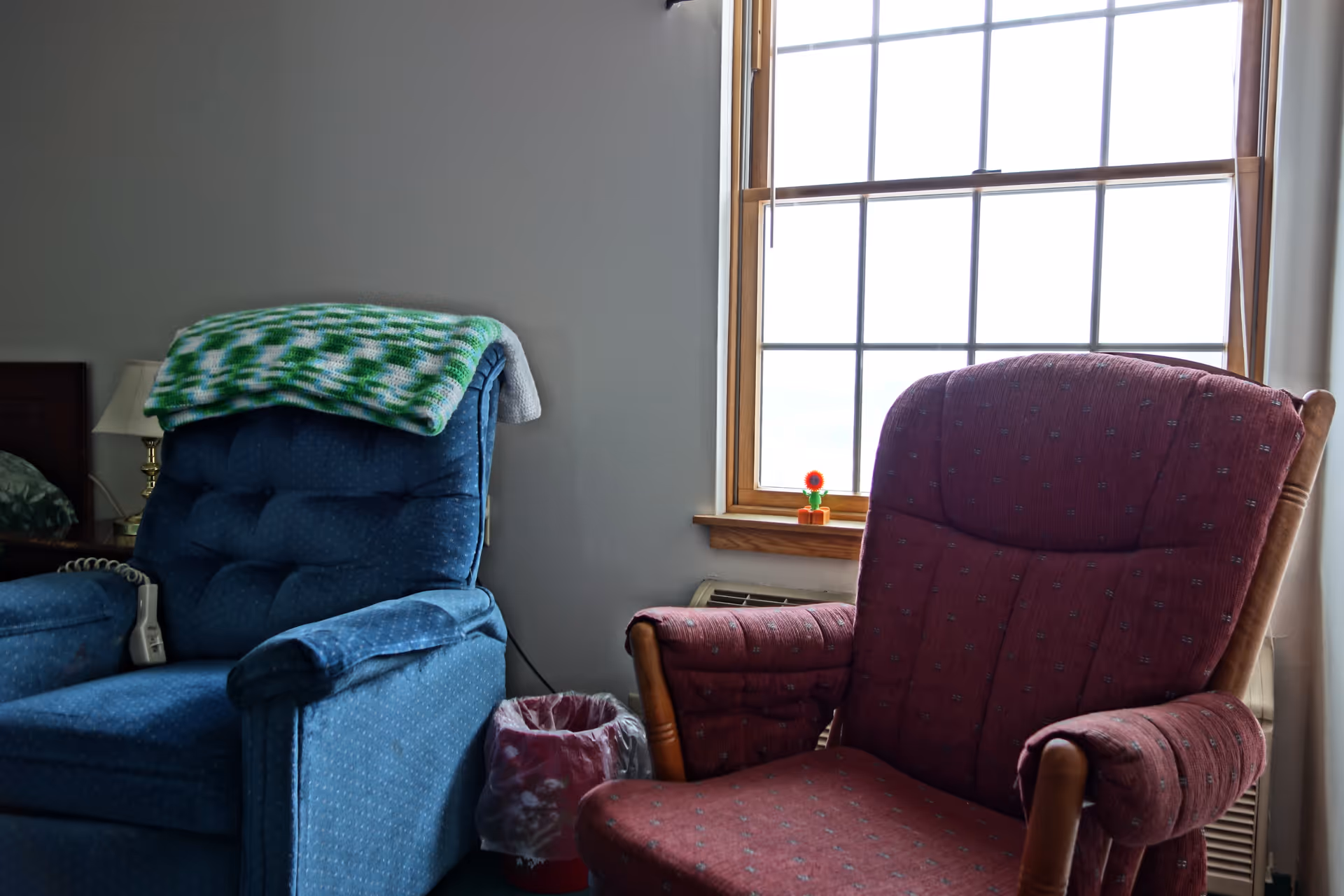 Two upholstered armchairs sit beside a window in a room, one with a green knit blanket draped over it.