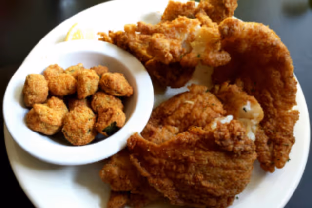A white plate with several pieces of fried catfish and a small white bowl filled with fried okra, with a lemon wedge partially visible on the side.