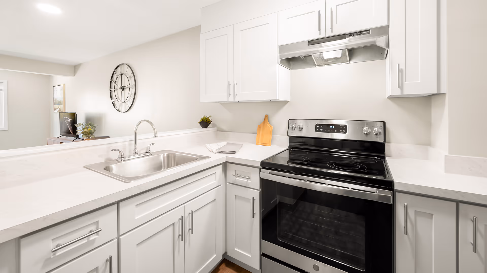 Bright modern kitchen with white cabinets, a stainless steel sink, and an electric range under a vent hood.