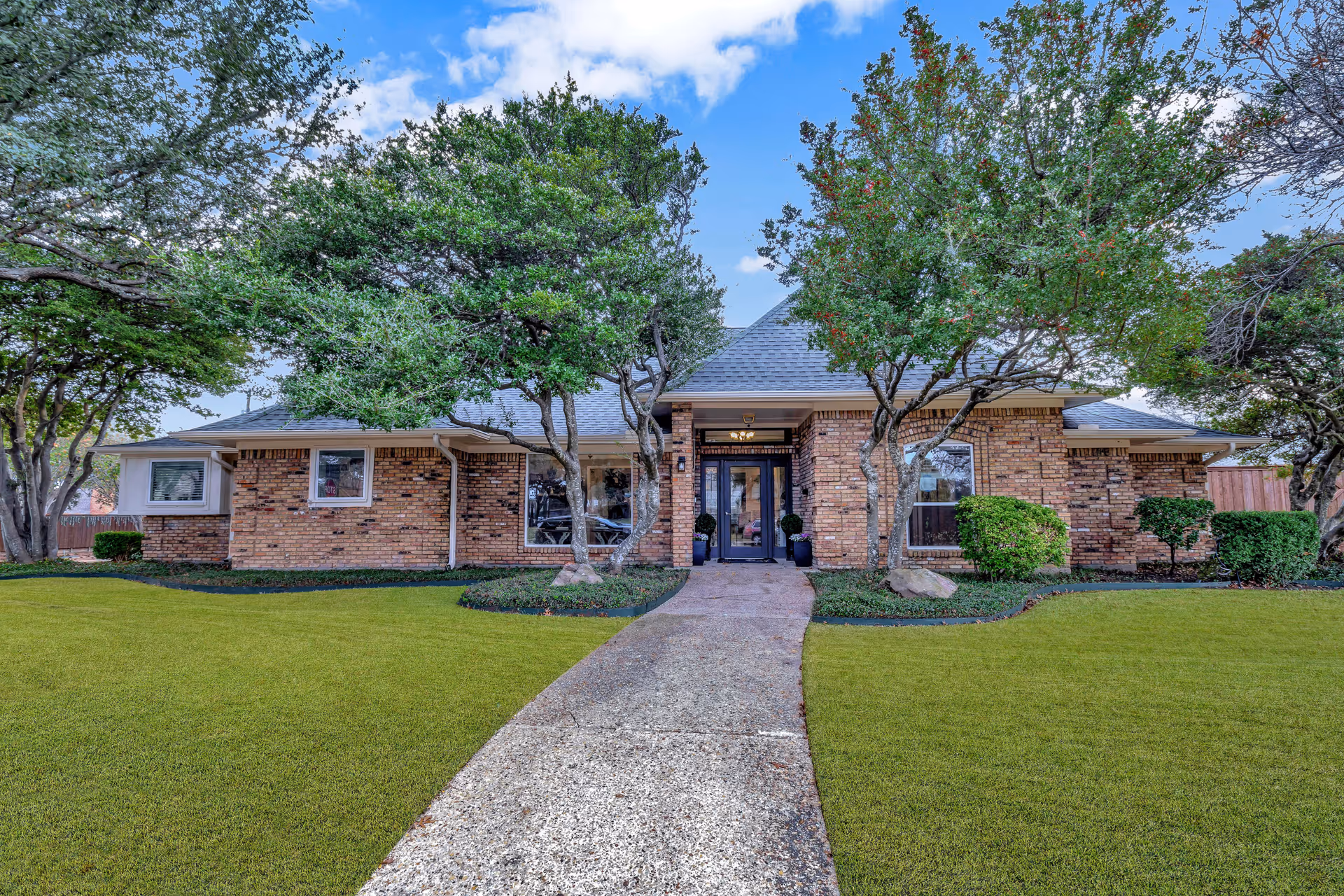 Front view of a single-story brick building with a central glass entrance, flanked by trees and a manicured lawn.