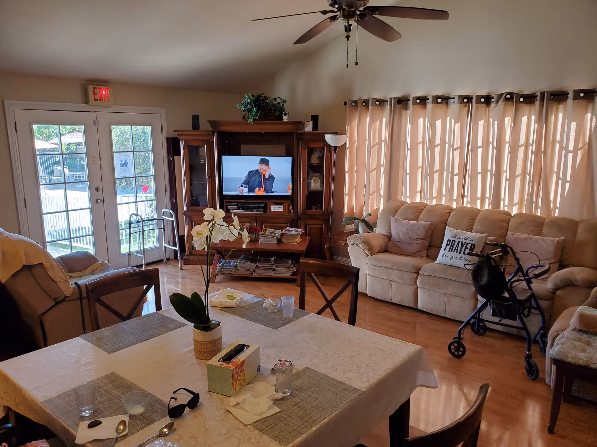 Open living room and dining area with a table in the foreground, TV and entertainment center, beige sofa, and a rollator near the couch.