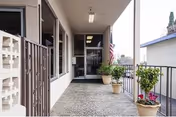 Covered outdoor walkway with potted plants along the railing leading to a glass door entrance of Del Mar Convalescent Hospital. An American flag is displayed near the entrance.