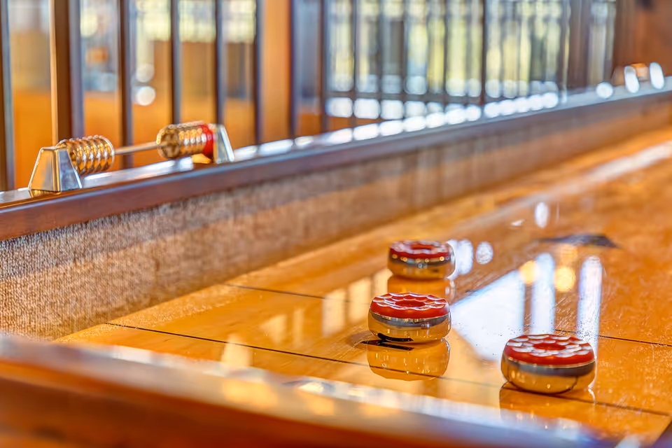A close-up view of a shuffleboard table featuring three pucks on a polished wooden surface, with a railing in the background.