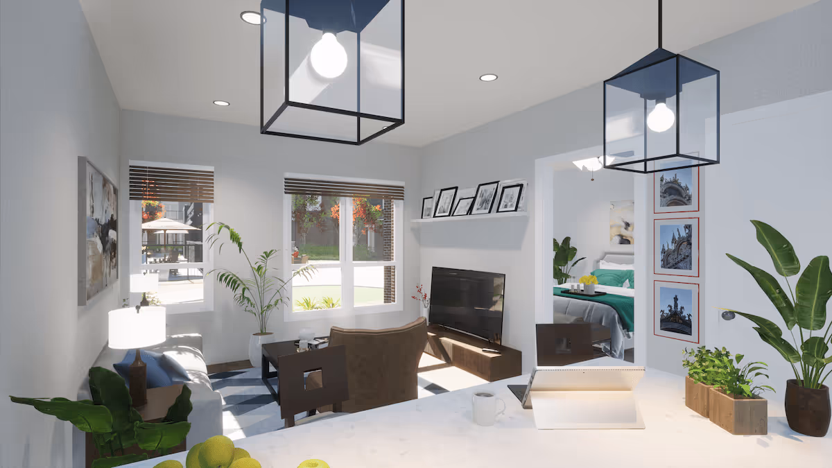 A bright and modern living room with large windows letting in natural light. The room features a sofa, a brown armchair, a coffee table, a flat-screen TV on a low stand, and framed photos on a shelf above the TV. There are two large pendant lights hanging from the ceiling. A view into a bedroom with a green bedspread is visible through an open doorway. The foreground shows a white countertop with a tablet, a coffee mug, and potted plants.