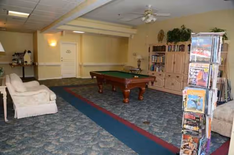 A spacious senior living lounge with a pool table, couches, and a magazine rack.