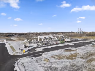 Aerial view of a newly constructed senior living facility building with multiple connected units, surrounded by paved parking areas and open land under a blue sky with some clouds.