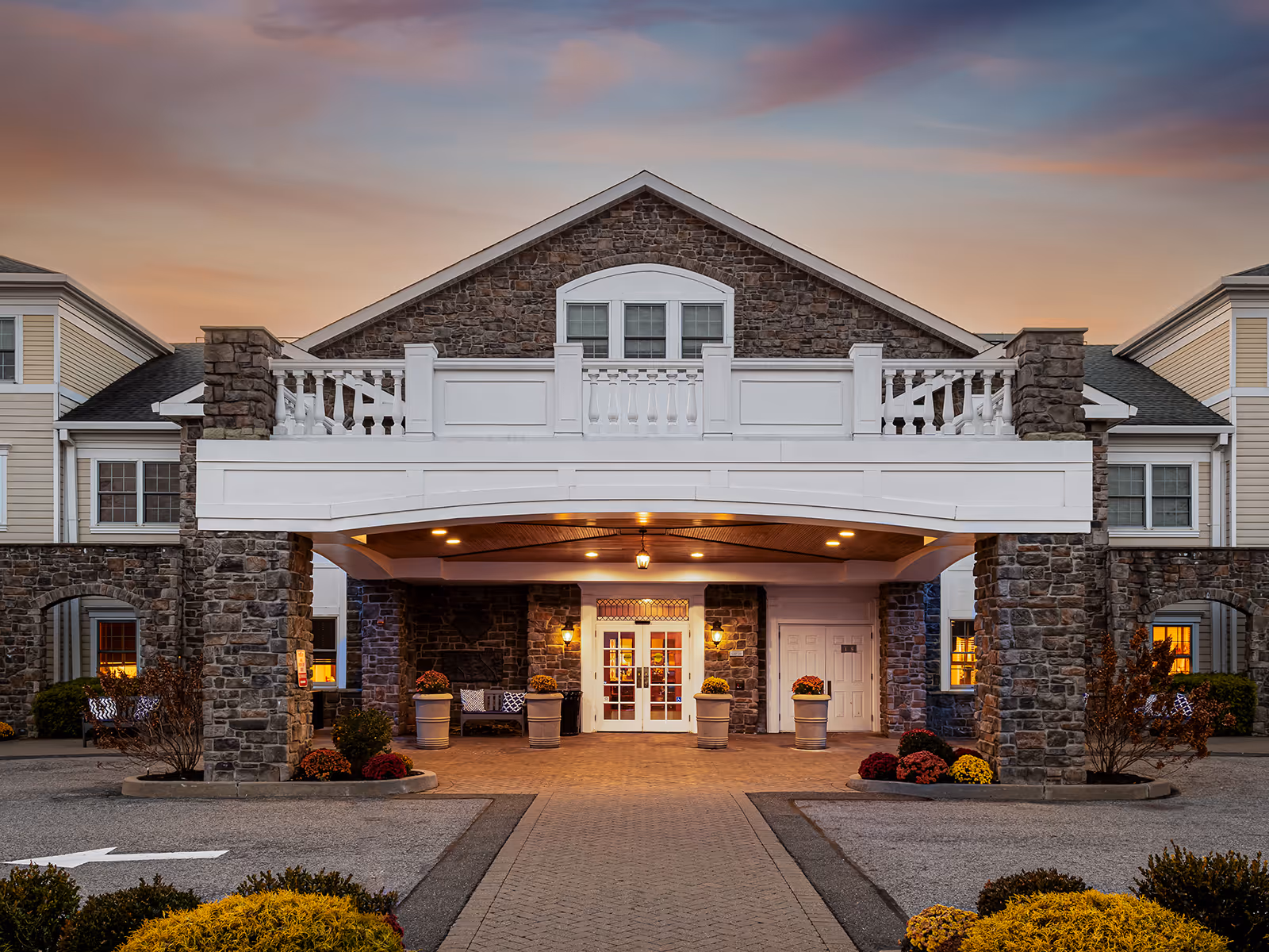 Exterior view of a stone-faced senior living facility front entrance at dusk.