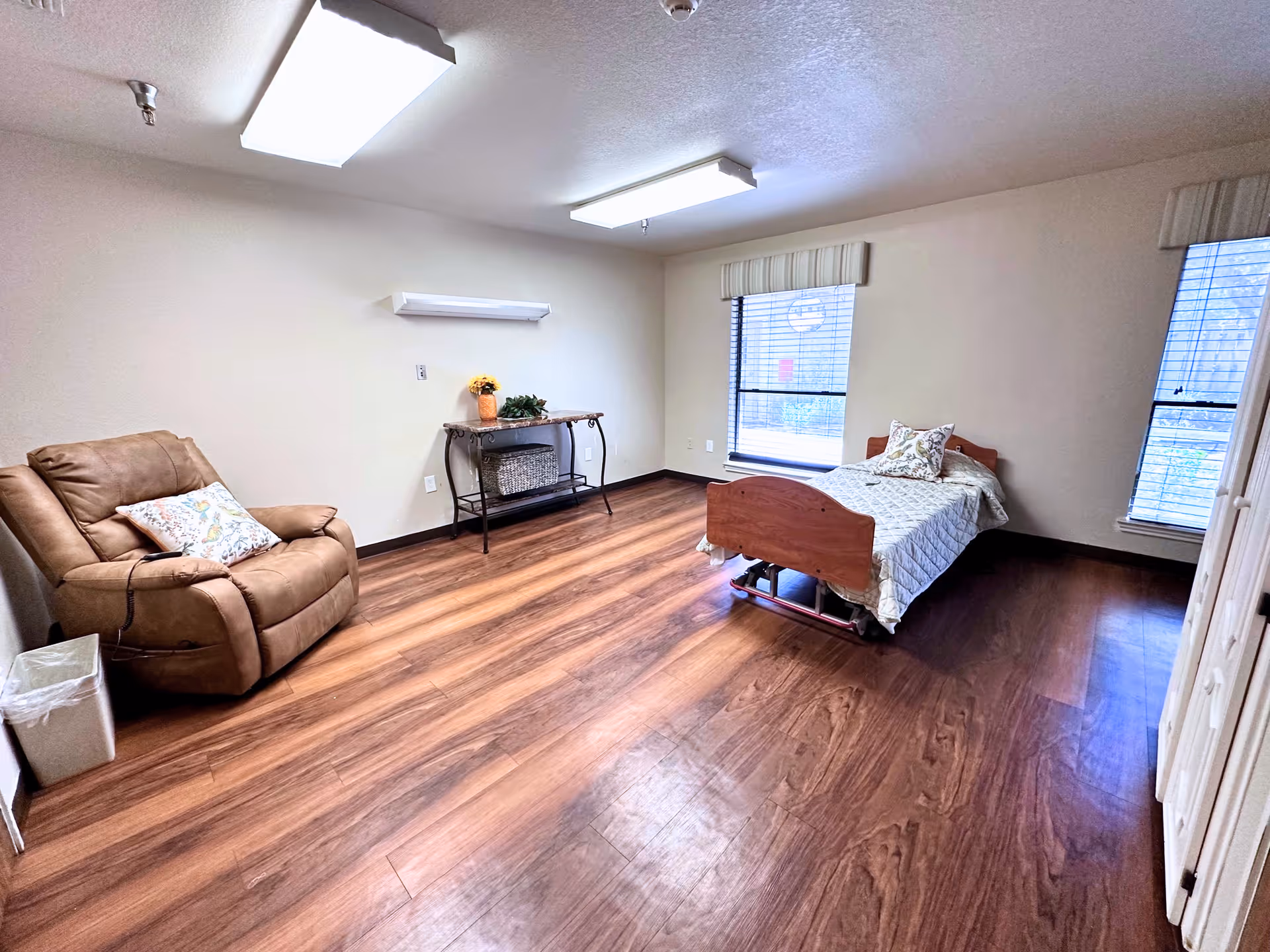 Spacious senior bedroom with a single bed, recliner, small side table and wood floors.
