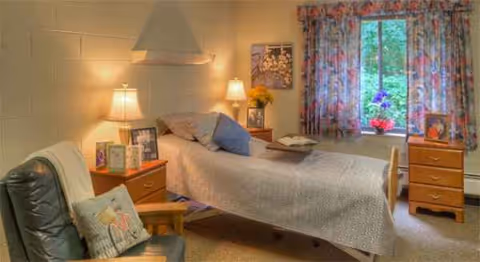 Cozy senior living facility bedroom featuring a bed, nightstands, and floral curtains.
