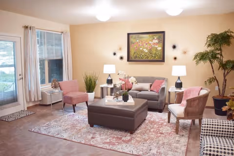 Comfortable living room with a sofa, armchairs, ottoman coffee table, lamps, plants, and wall art.