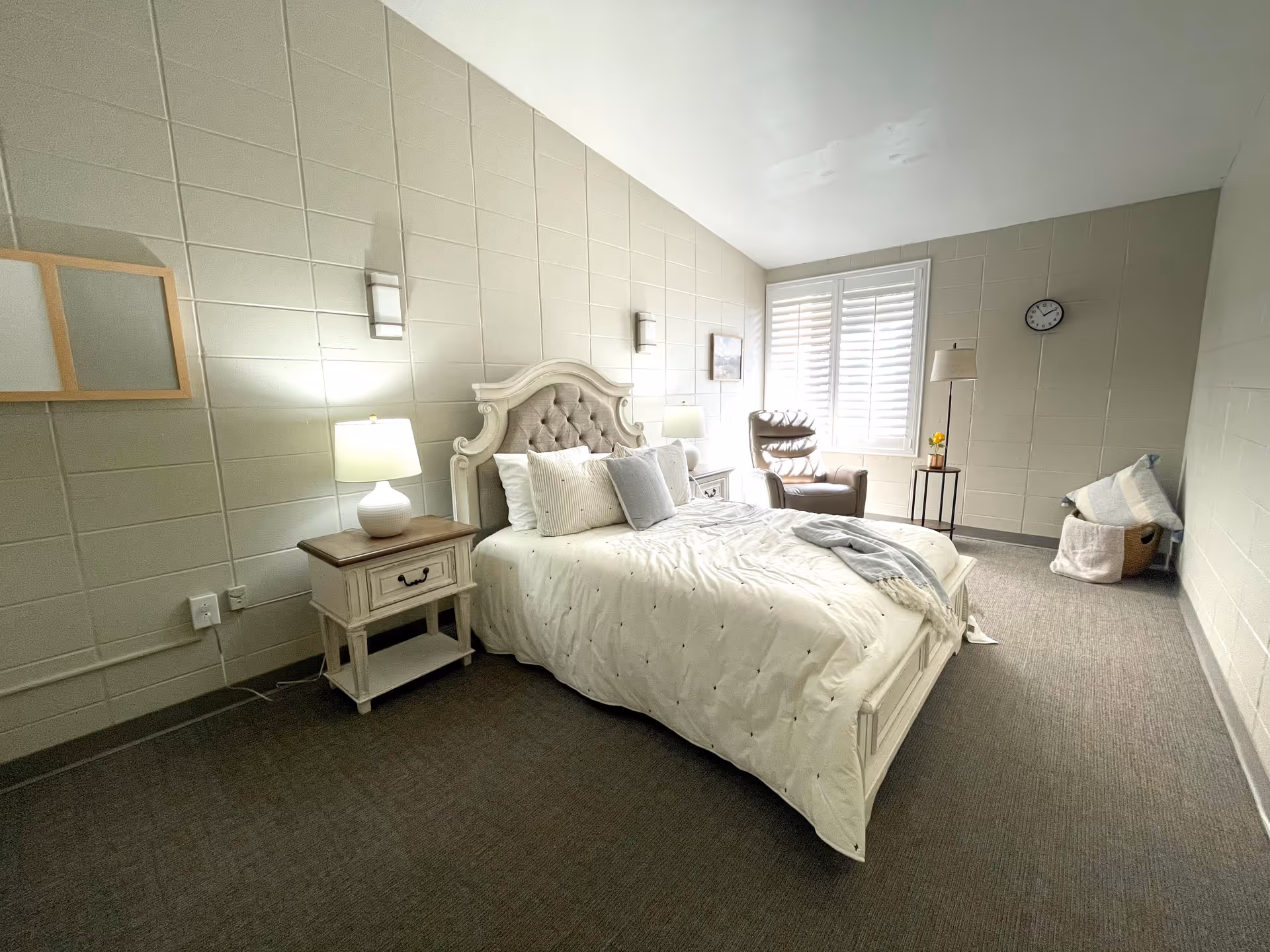 Elegant bedroom in a senior living facility with tufted bed, nightstands, and window seating.