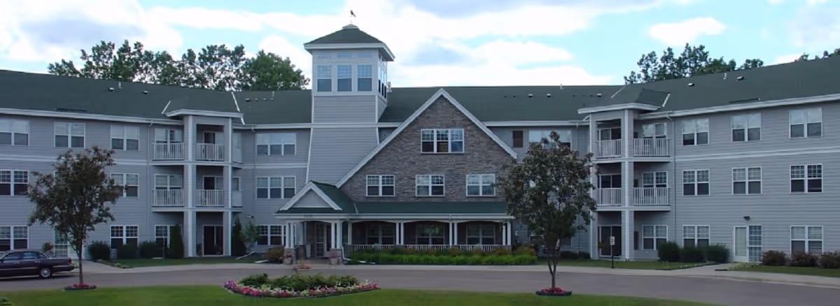 Front exterior view of Cardinal Pointe of Maplewood, a three-story senior living facility with a central tower, multiple windows, balconies, and landscaped grounds including trees and flower beds.
