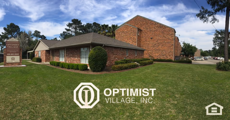 Brick single- and two-story senior living buildings with a manicured lawn and an Optimist Village sign under a blue sky.