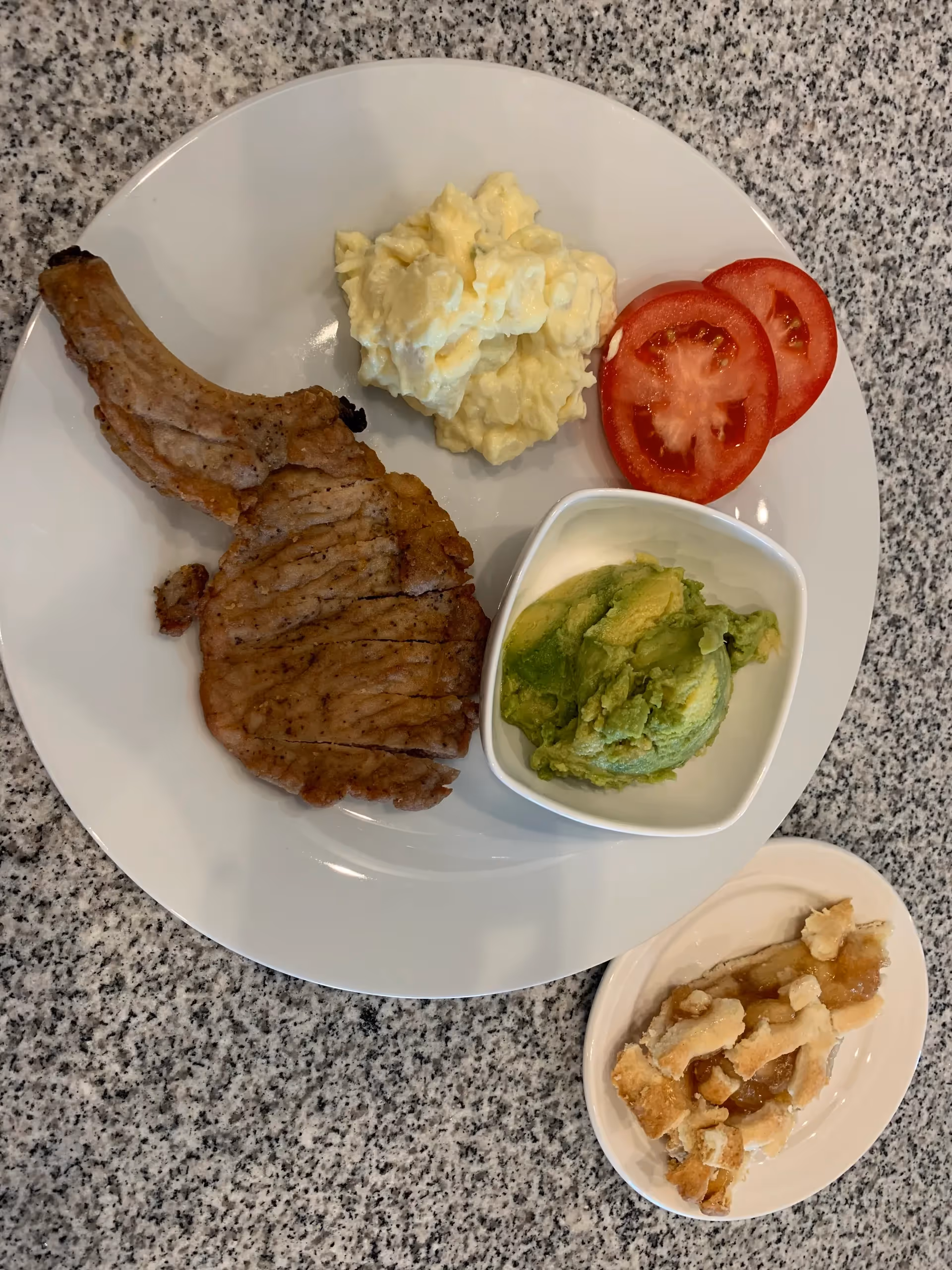 Plate with grilled meat, mashed potatoes, avocado, tomato slices, and dessert.