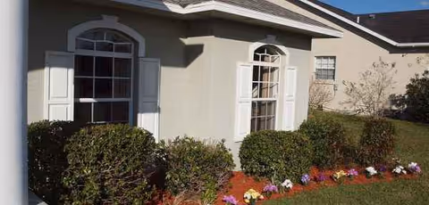 Front exterior of Ellison Adult Family Care Home with hedges and colorful flowers.