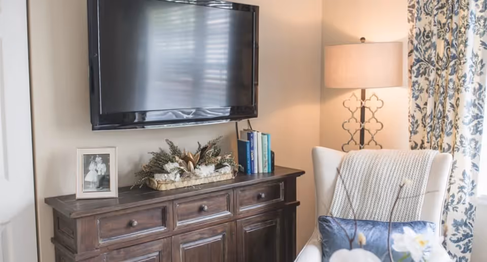 Cozy living room corner with a wall-mounted TV above a wooden console, decorative accents, a floor lamp, and an upholstered armchair.