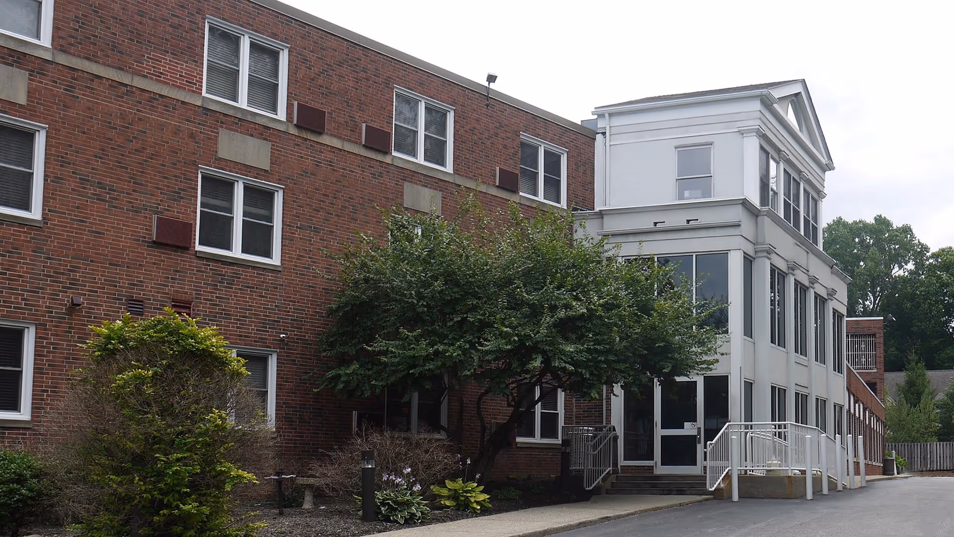 Brick senior living building with a white glass-front entrance and surrounding trees.