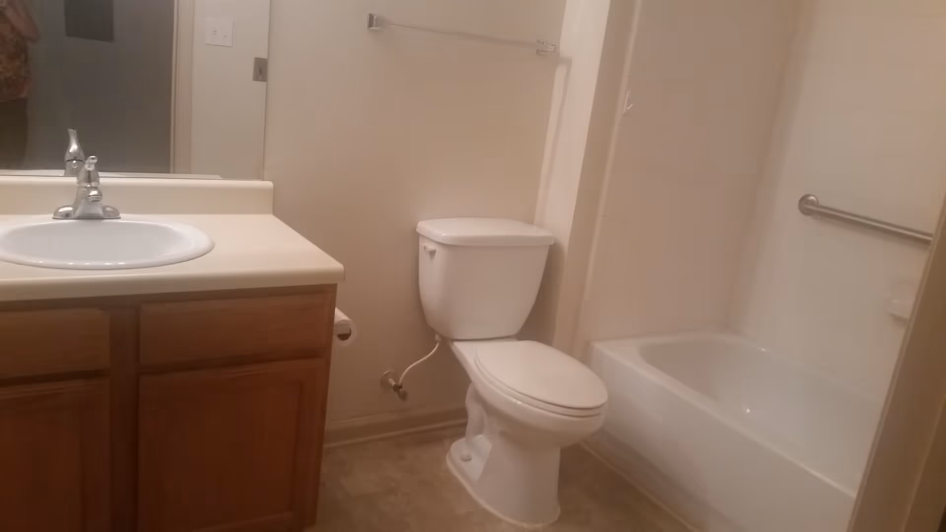 A bathroom with a white sink and faucet on a wooden cabinet, a white toilet, and a white bathtub with a grab bar on the tiled wall.