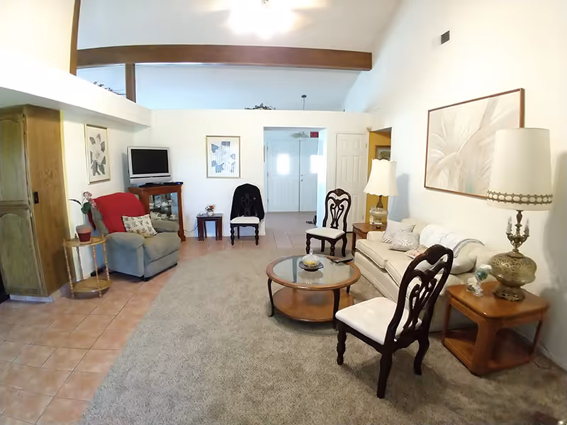 Bright living room with a sofa, armchairs, coffee table, TV and lamps under a vaulted ceiling with exposed beam.