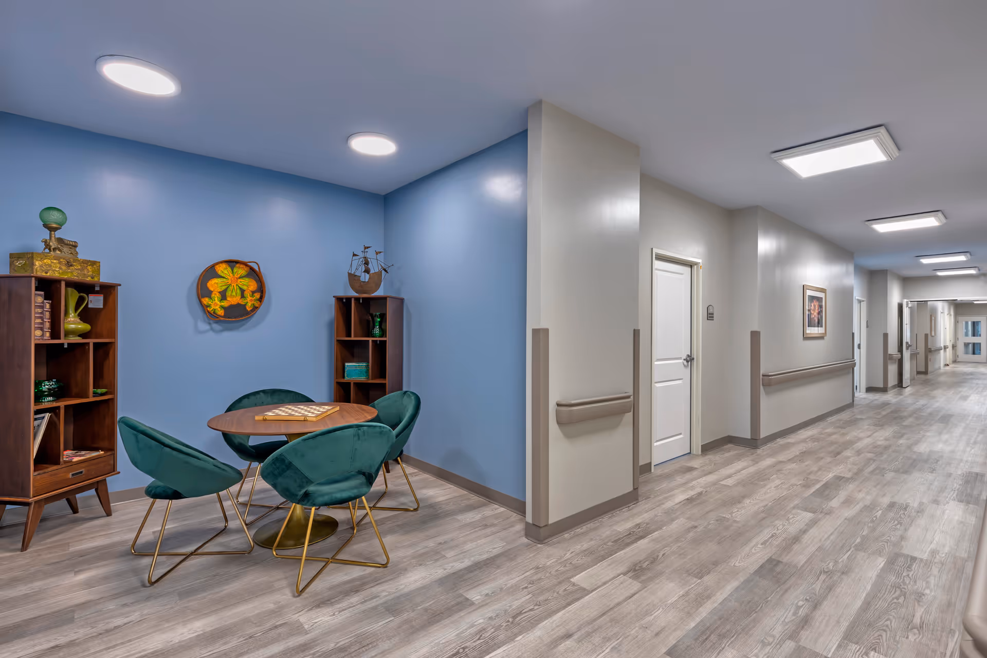A bright interior corridor with a small seating area of green chairs and a round table against a blue accent wall.