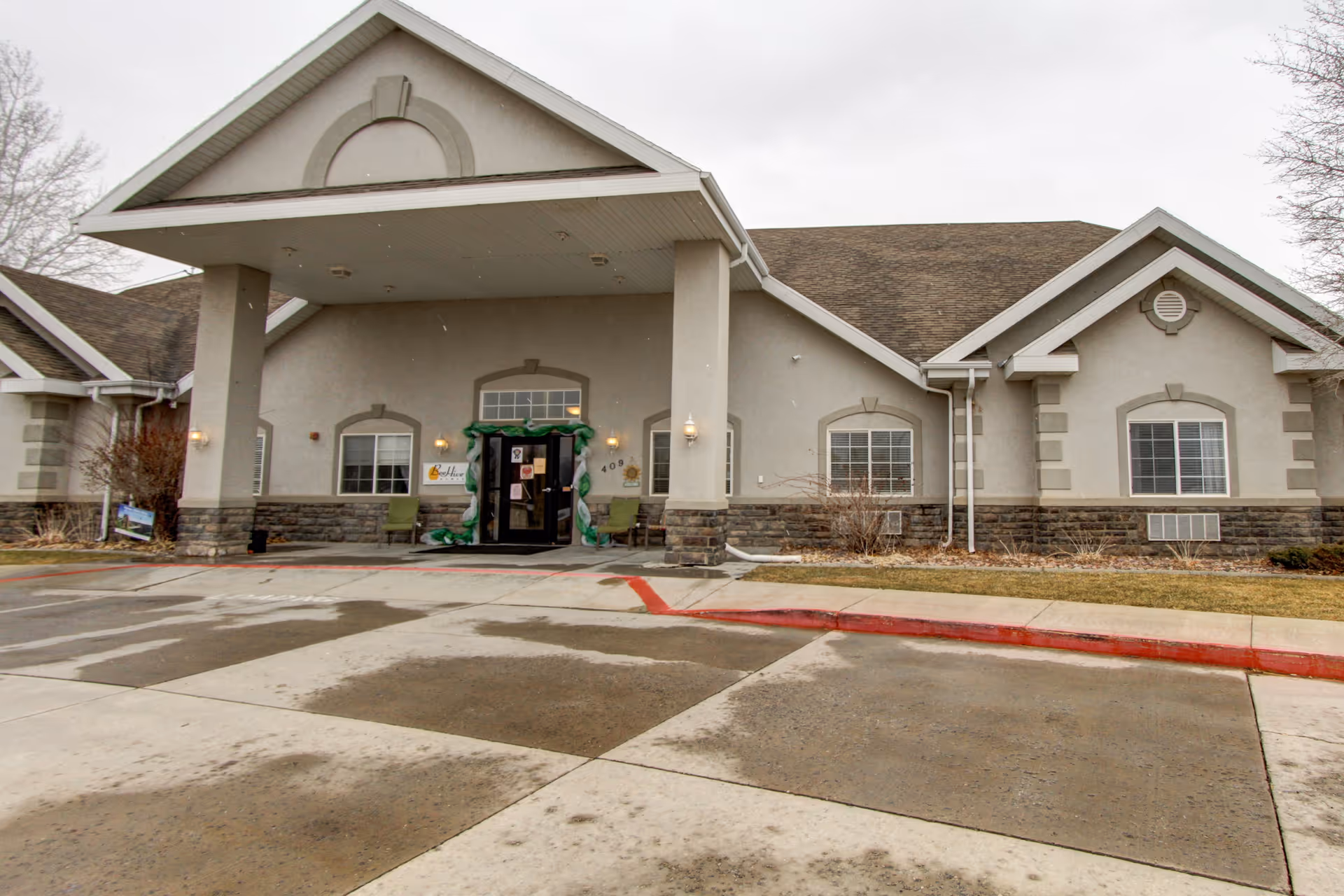 Front exterior of a one-story senior living facility with a covered entrance, windows, and driveway.