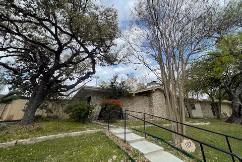 Stone-clad senior living building exterior with entrance stairs, railing, and trees
