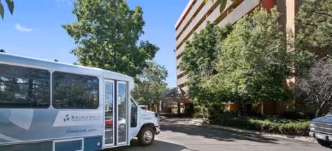 Shuttle bus at Brookdale Tamarac Square entrance beside trees and a multi-story building.