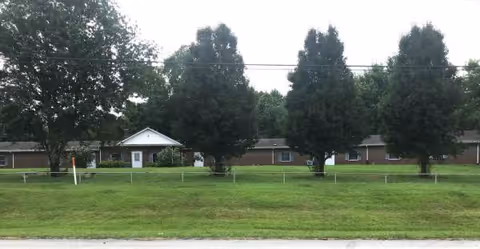 Front exterior of a single-story brick senior home with a grassy lawn and trees.