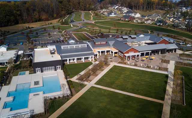 Aerial view of the Trilogy Lake Norman senior living campus with buildings, outdoor pool, large lawns, walkways and nearby houses.