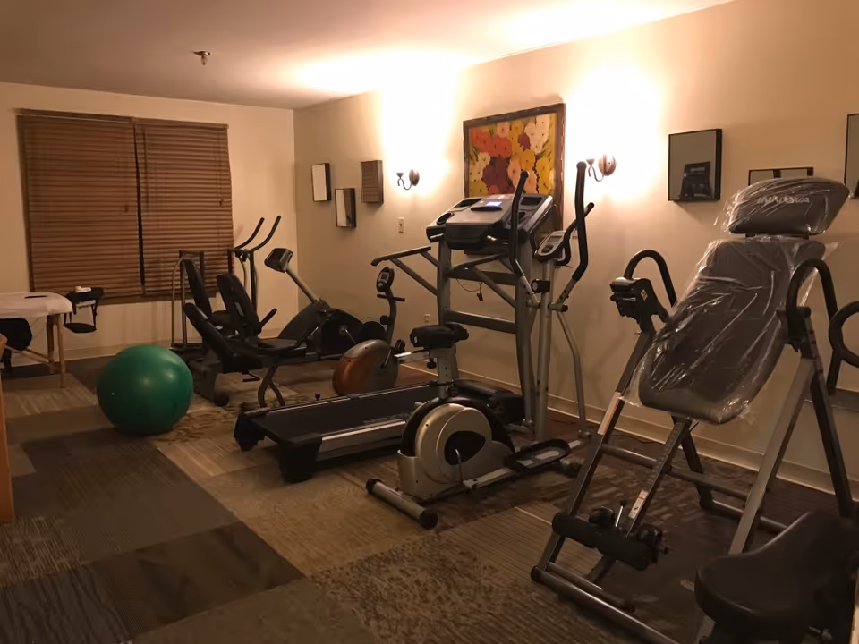 Small fitness room with treadmills, exercise bikes, an inversion bench and a green exercise ball.