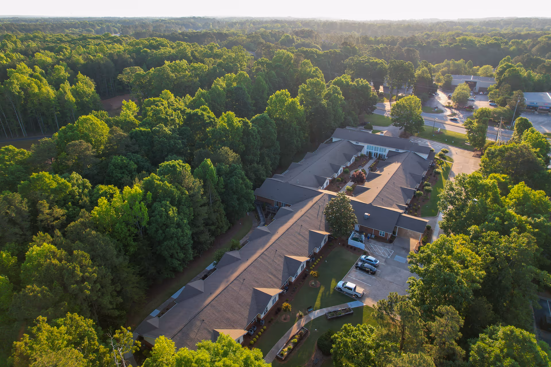 Aerial view of a senior living facility building surrounded by dense trees and a parking area.