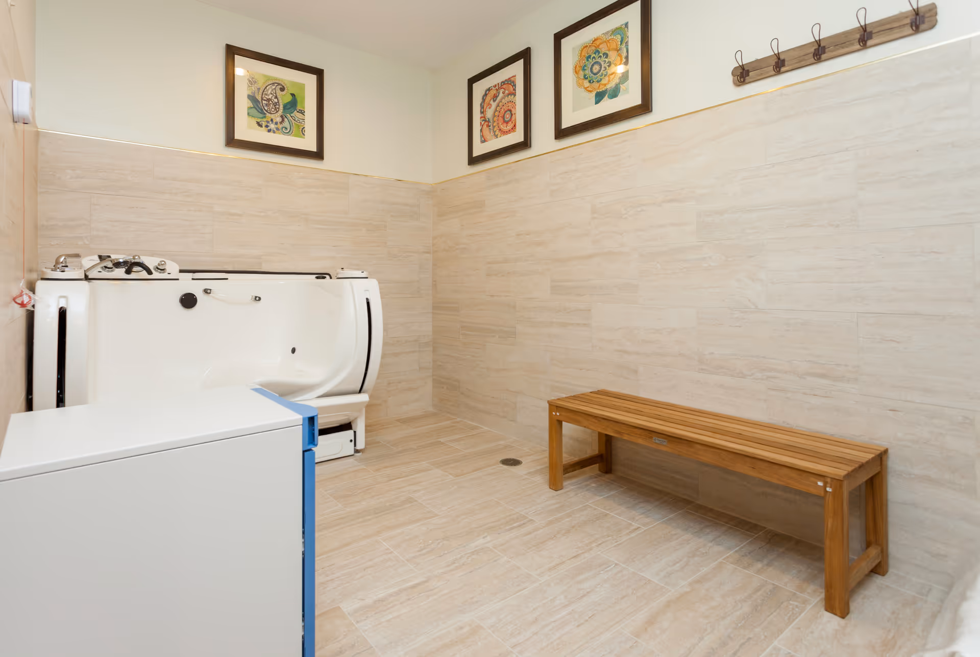 Accessible bathing room with a walk-in tub, wooden bench, tiled walls, and framed artwork.