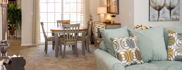 Cozy living area with sofa, decorative cushions, dining table, and natural light from large window.